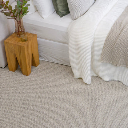 Bedroom with a bed, wooden side table, and white carpet.