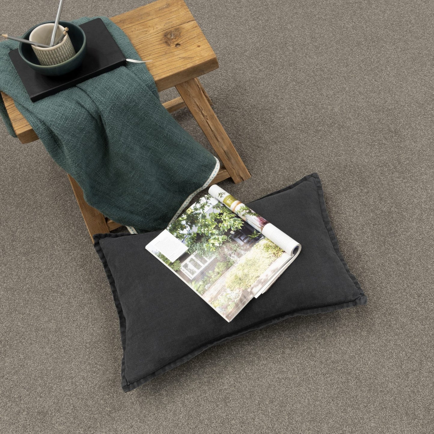 Gray carpet with a wooden stool, green blanket, and magazine on a gray floor.