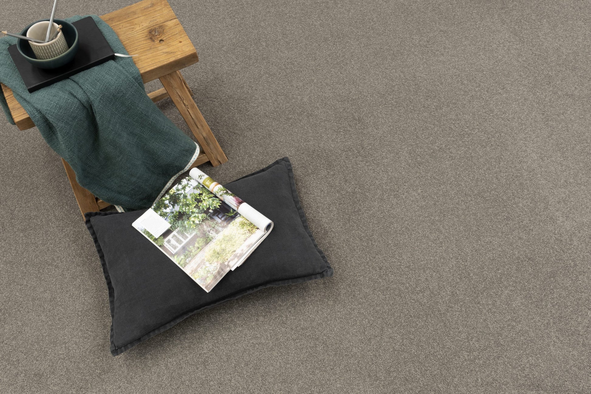 Gray carpet with a wooden stool, green blanket, and magazine on a gray floor.