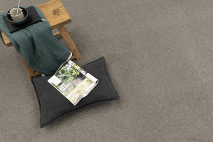 Gray carpet with a wooden stool, green blanket, and magazine on a gray floor.