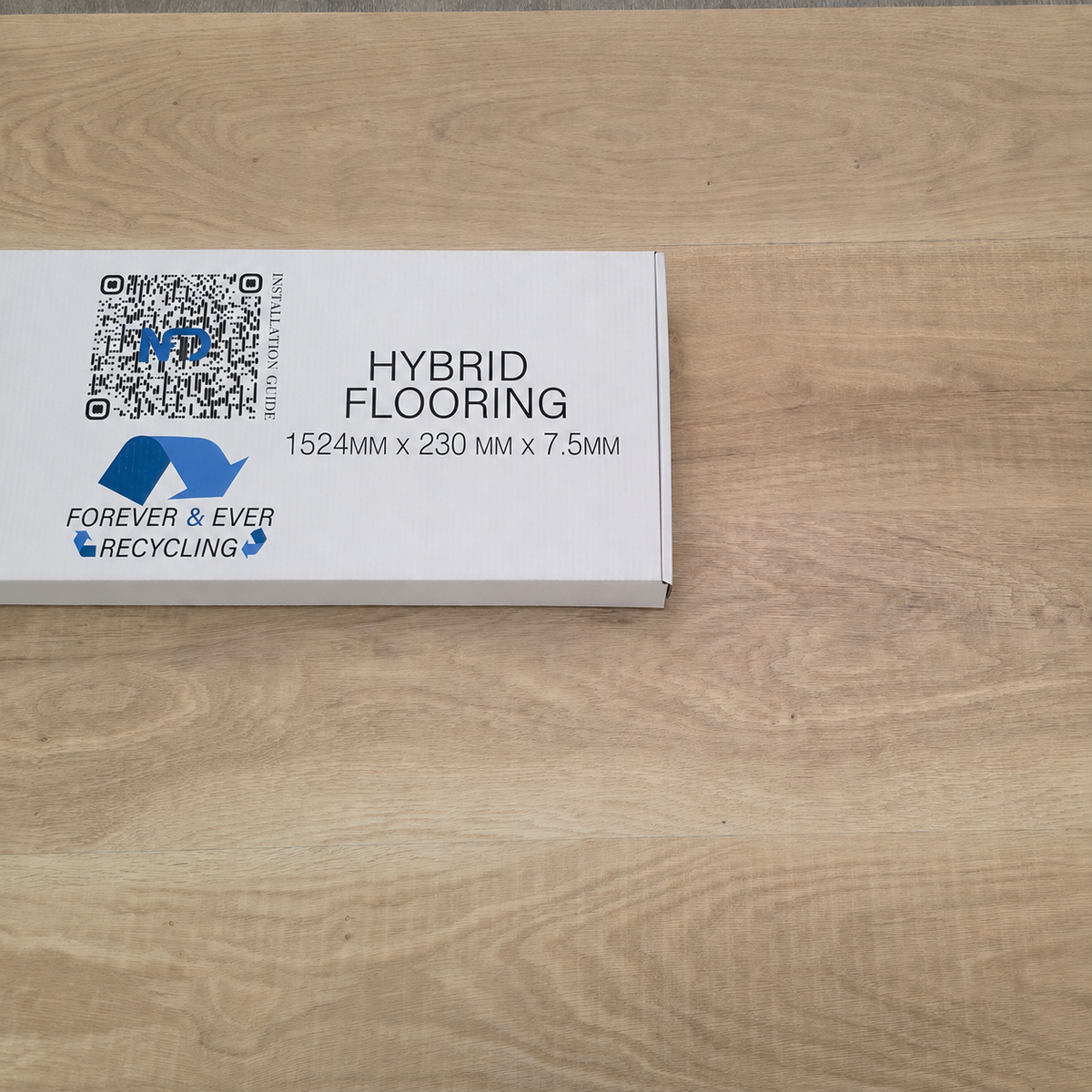 A white product box labeled 'HYBRID FLOORING 1524MM X 230 MM X 7.5MM' with blue Forever & Ever Recycling branding, placed on a light wood flooring surface.