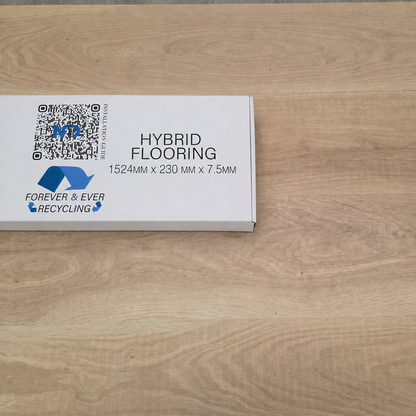 A white product box labeled 'HYBRID FLOORING 1524MM X 230 MM X 7.5MM' with blue Forever & Ever Recycling branding, placed on a light wood flooring surface.