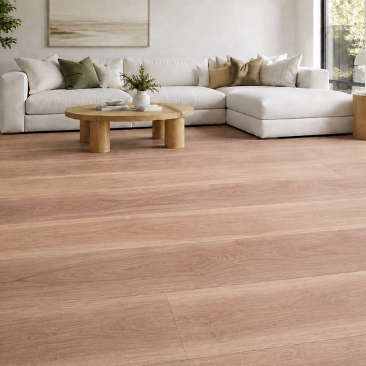 Light oak wood look hybrid plank flooring shown in a modern, bright living room with a white sectional sofa, wooden coffee table, and large windows.